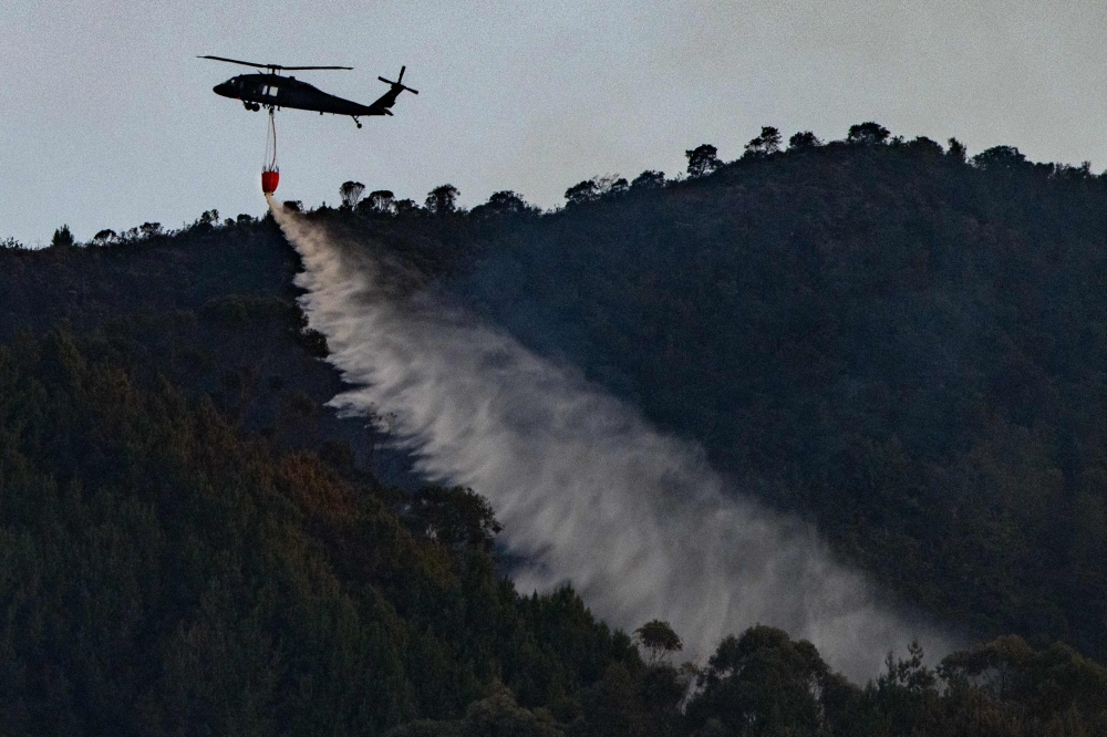 A helicopter from the Colombian Police drops water to put out a forest fire in Bogota on January 24, 2024. (Photo by Luis Acosta / AFP)
 