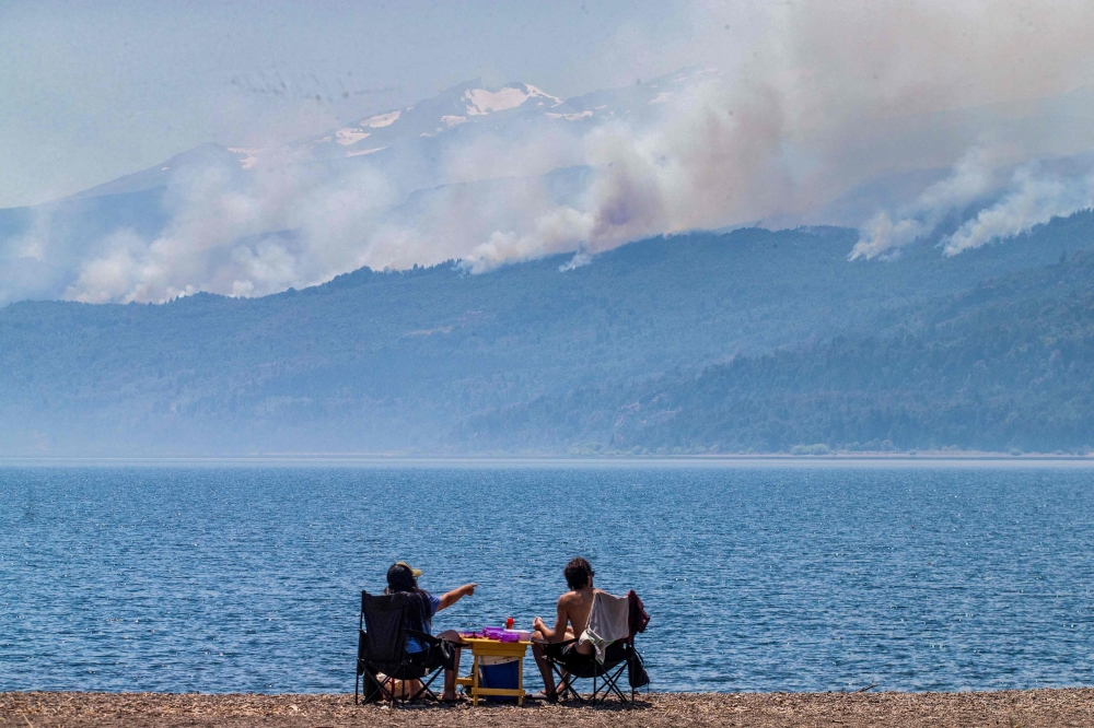 A picture released by Telam news agency shows tourists looking at smoke billowing from a forest fire at Los Alerces National Park in Chubut province, Argentina, on January 28, 2024. Photo by MARTIN LEVICOY / TELAM / AFP
