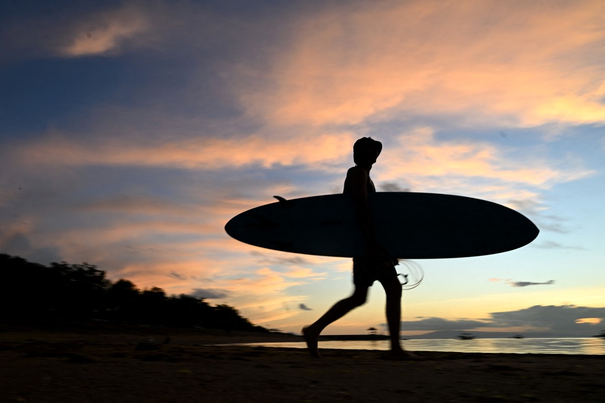 A surfer walks to the sea during sunrise at Sanur beach on the Indonesian resort island of Bali on February 6, 2024. (Photo by SONNY TUMBELAKA / AFP)
