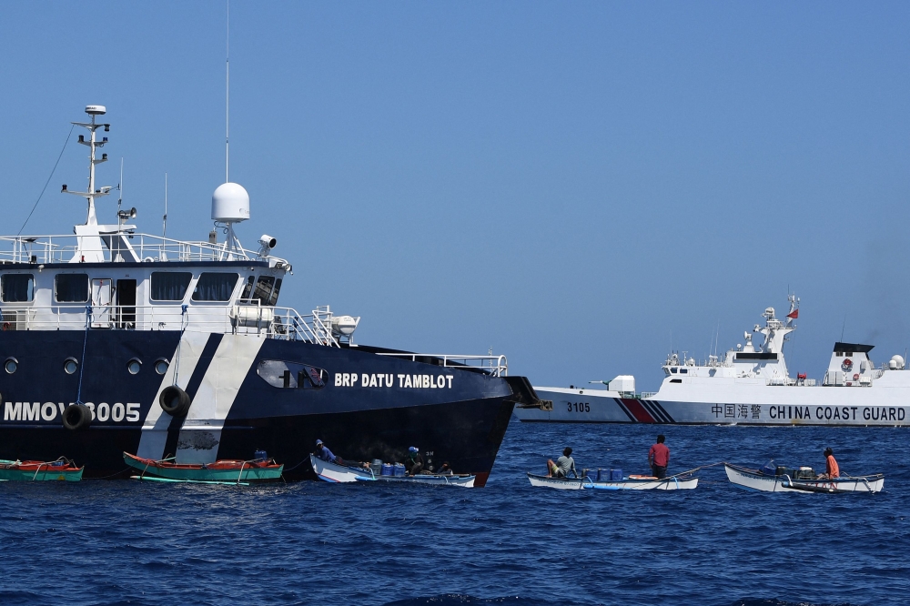 This photo taken on February 15, 2024 shows Filipino fishermen aboard their wooden boats queueing for free fuel beside the Philippine Bureau of Fisheries and Aquatic Resources (BFAR) ship BRP Datu Tamblot (L) as a Chinese coast guard ship (background R) monitors near the China-controlled Scarborough Shoal, in disputed waters of the South China Sea. (Photo by Ted Aljibe / AFP)