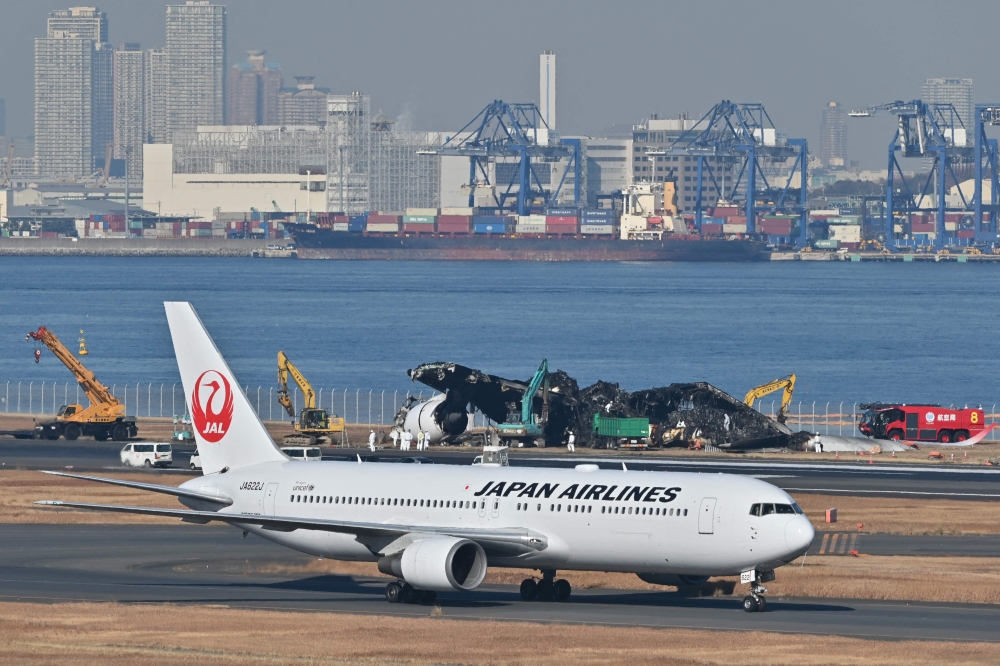 A Japan Airlines (JAL) plane taxis past as officials remove the remaining debris of a JAL passenger plane from the runway area at Tokyo International Airport at Haneda on January 5, 2024. Photo by Richard A. BROOKS / AFP

