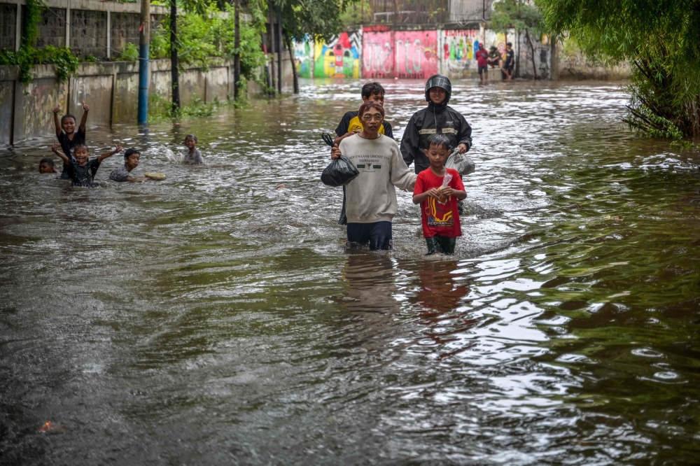 People walk through floodwaters due to heavy rainfall in a residential area in Jakarta on February 29, 2024. (Photo by BAY ISMOYO / AFP)