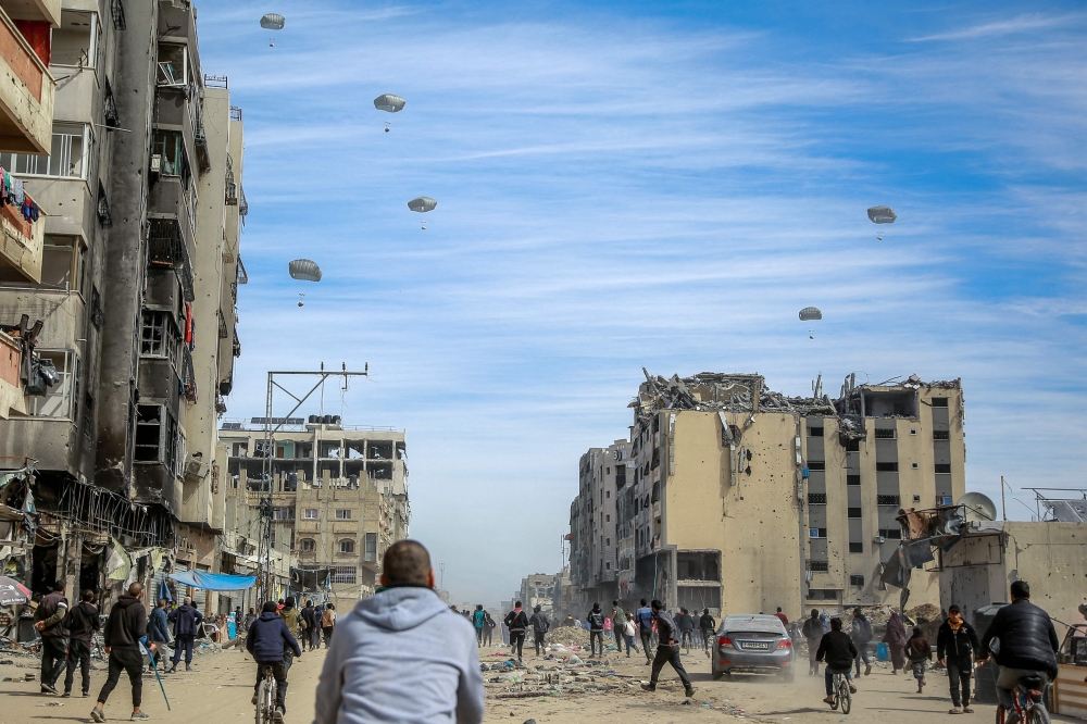 Palestinians run along a street as humanitarian aid is airdropped in Gaza City on March 1, 2024.  (Photo by AFP)