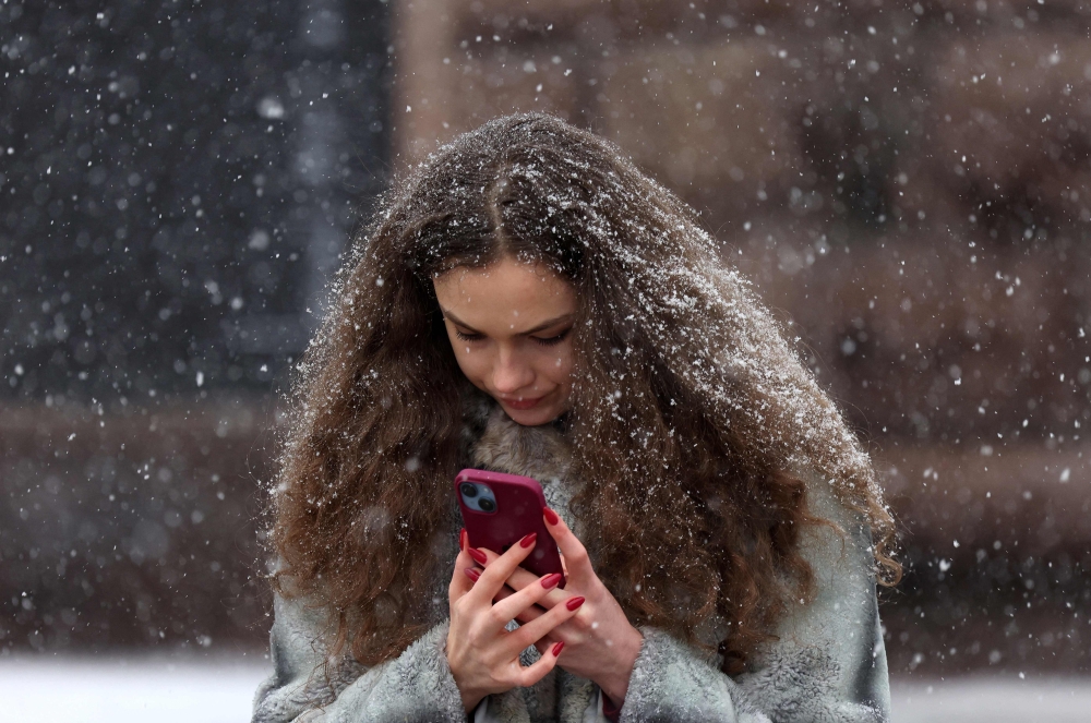 A young woman looks at her smartphone during snowfall in Kyiv, on March 12, 2024, amid the Russian invasion of Ukraine. (Photo by Anatolii STEPANOV / AFP)
