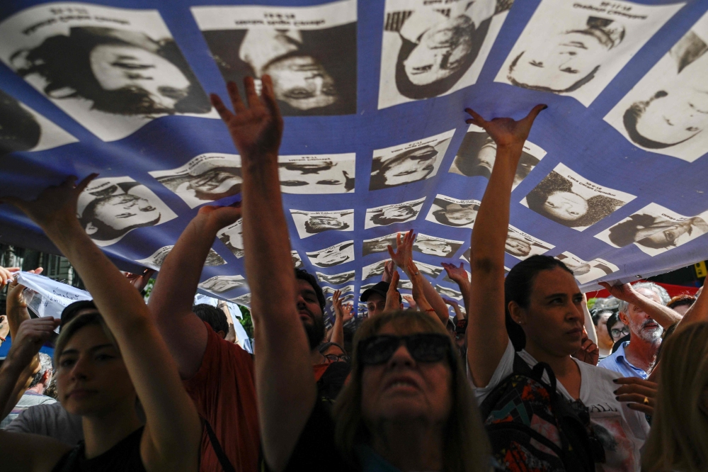 Hundreds hold a large banner with portraits of people who disappeared during the military dictatorship (1976-1983) while heading to Plaza de Mayo Square to commemorate the 48th anniversary of the coup in Buenos Aires on March 24, 2023. (Photo by Luis ROBAYO / AFP)
