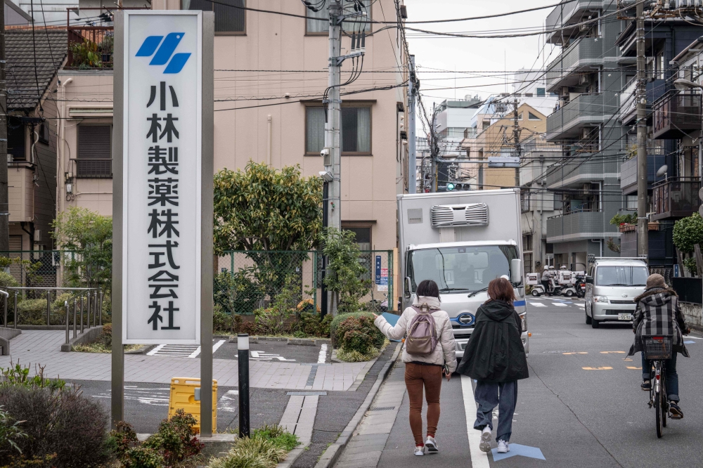 A woman points her finger at the signage of Kobayashi Pharmaceutical as she walks past the company's office in Tokyo on March 28, 2024. Photo by Yuichi YAMAZAKI / AFP
