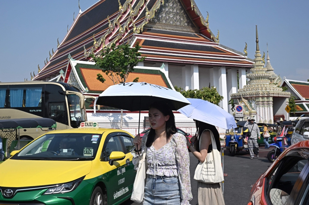 (Files) Tourists shield themselves from the sun with umbrellas to combat the heat outside Wat Pho Buddhist temple in Bangkok on April 1, 2024. (Photo by Lillian Suwanrumpha / AFP)
