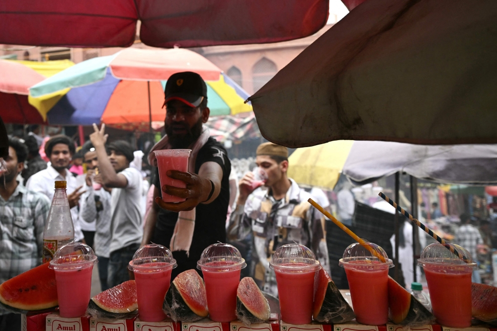A fruit juice vendor displays a drink to customers during a hot summer day in the old quarters of New Delhi on May 17, 2024. (Photo by Arun Sankar / AFP)