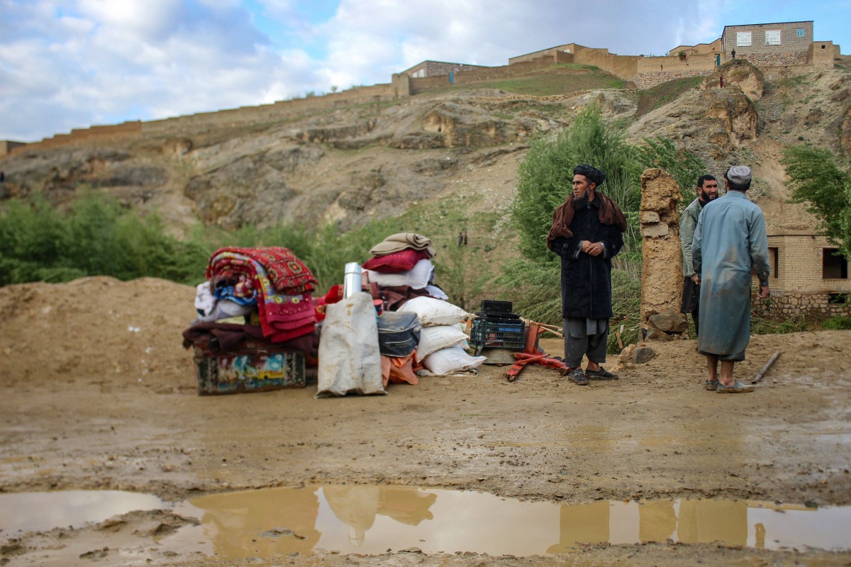 Afghan men stand beside their belongings kept near a damaged house after flash floods following heavy rainfall in Firozkoh, Ghor province on May 18, 2024. Flash flooding has killed at least 50 people in western Afghanistan, provincial police said on May 18, a week after hundreds were washed away in the north of the country. (Photo by AFP)
