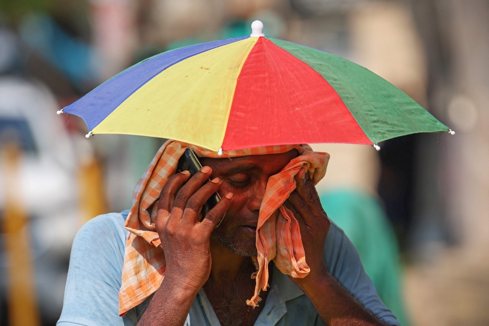 A vendor with an umbrella over his head talks on mobile phone as he wipes his face with a cloth on a hot summer day in Varanasi on May 27, 2024. Photo by Niharika KULKARNI / AFP