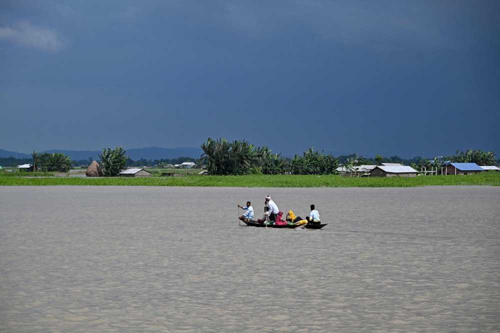 People wade through flood waters on a boat at Lehpati village of Morigaon district in India's northeastern state of Assam on July 3, 2024. (Photo by Biju Boro / AFP)