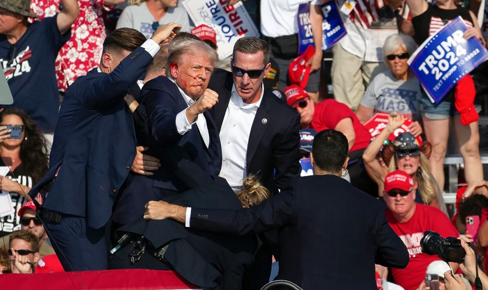 File: Republican candidate Donald Trump is seen with blood on his face surrounded by secret service agents as he is taken off the stage. (Photo by Rebecca Droke / AFP)