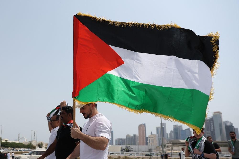 A man holding a Palestinian flag walks with others towards the Imam Muhammad bin Abdul Wahhab Mosque in Doha to bid farewell Hamas leader Ismail Haniyeh after his killing in Tehran. Photo by KARIM JAAFAR / AFP