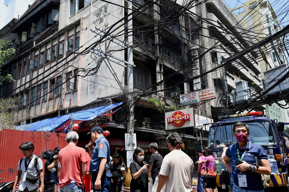 People, policemen, and media personnel are seen at the scene of a fire that ripped through a building in Manila's Chinatown on August 2, 2024. (Photo by Jam Sta Rosa / AFP)
