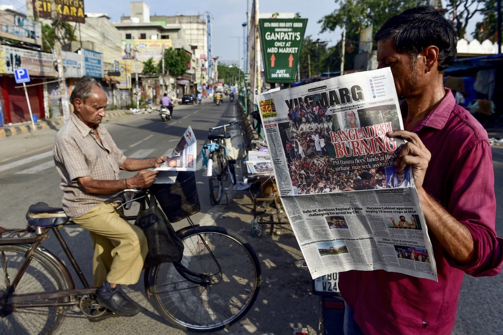 A man (R) reads a newspaper with an article on Bangladesh published on its front page, along a street in Jalandhar on August 6, 2024, a day after Bangladesh's Prime Minister Sheikh Hasina was ousted by anti-government protestors. Photo by Shammi MEHRA / AFP