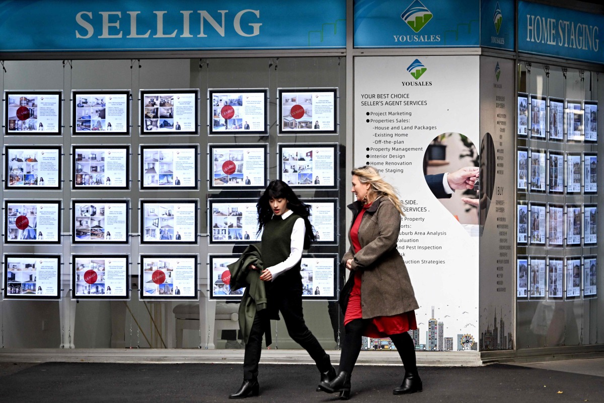People walk past a real estate agents display in Melbourne on August 6, 2024. (Photo by William WEST / AFP)