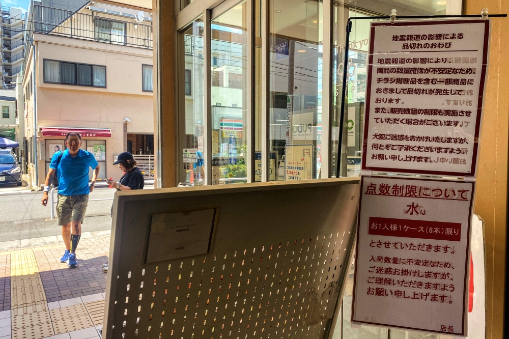 Customers walk by the entrance of a supermarket as signs written 