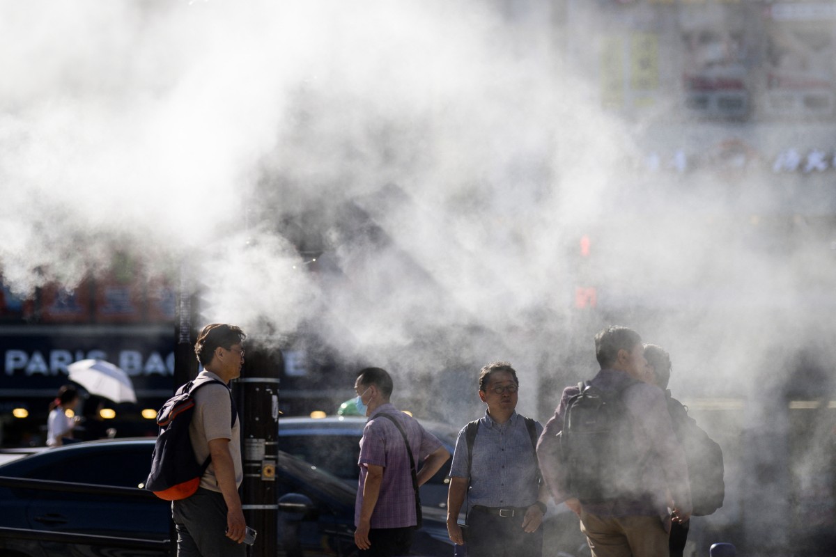 Pedestrians wait to cross a road as a cooling water mist is sprayed from nearby pipes in Busan on September 4, 2024. (Photo by ANTHONY WALLACE / AFP)
