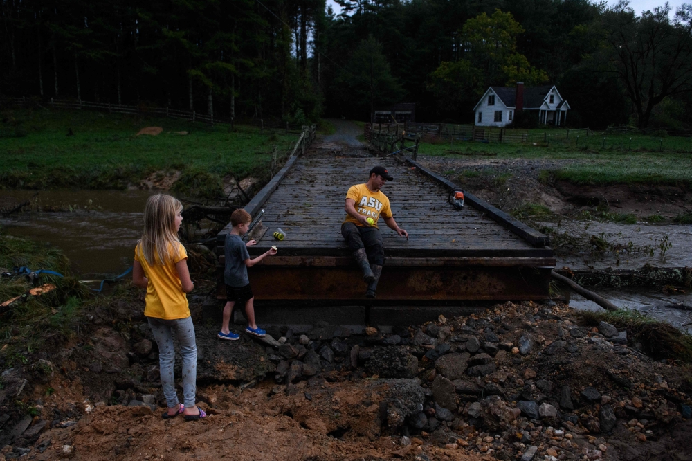 A man and his kids take a break from working on a washed out road to their home in Watauga County, North Carolina on September 27, 2024. (Photo by Melissa Sue Gerrits / GETTY IMAGES NORTH AMERICA / Getty Images via AFP)
