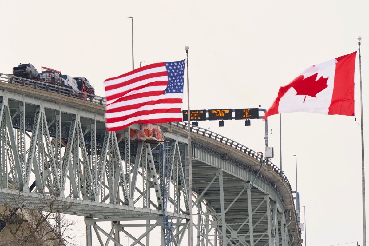 (FILES) The US and Canadian flags fly on the US side of the St. Clair River near the Bluewater Bridge border crossing between Sarnia, Ontario and Port Huron, Michigan on January 29, 2025. (Photo by Geoff Robins / AFP)
