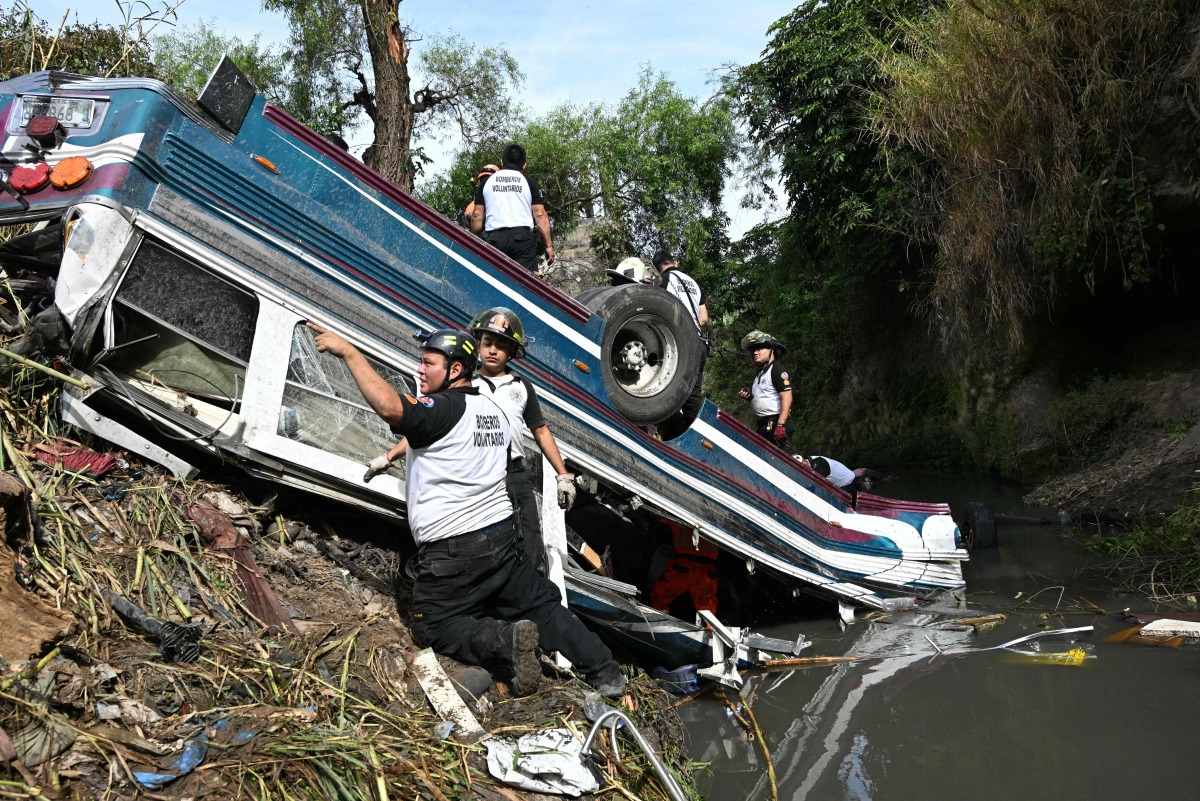 Volunteer firefighters work at the scene of an accident in which a bus fell down a ravine in Guatemala City on February 10, 2025. (Photo by Johan ORDONEZ / AFP)
