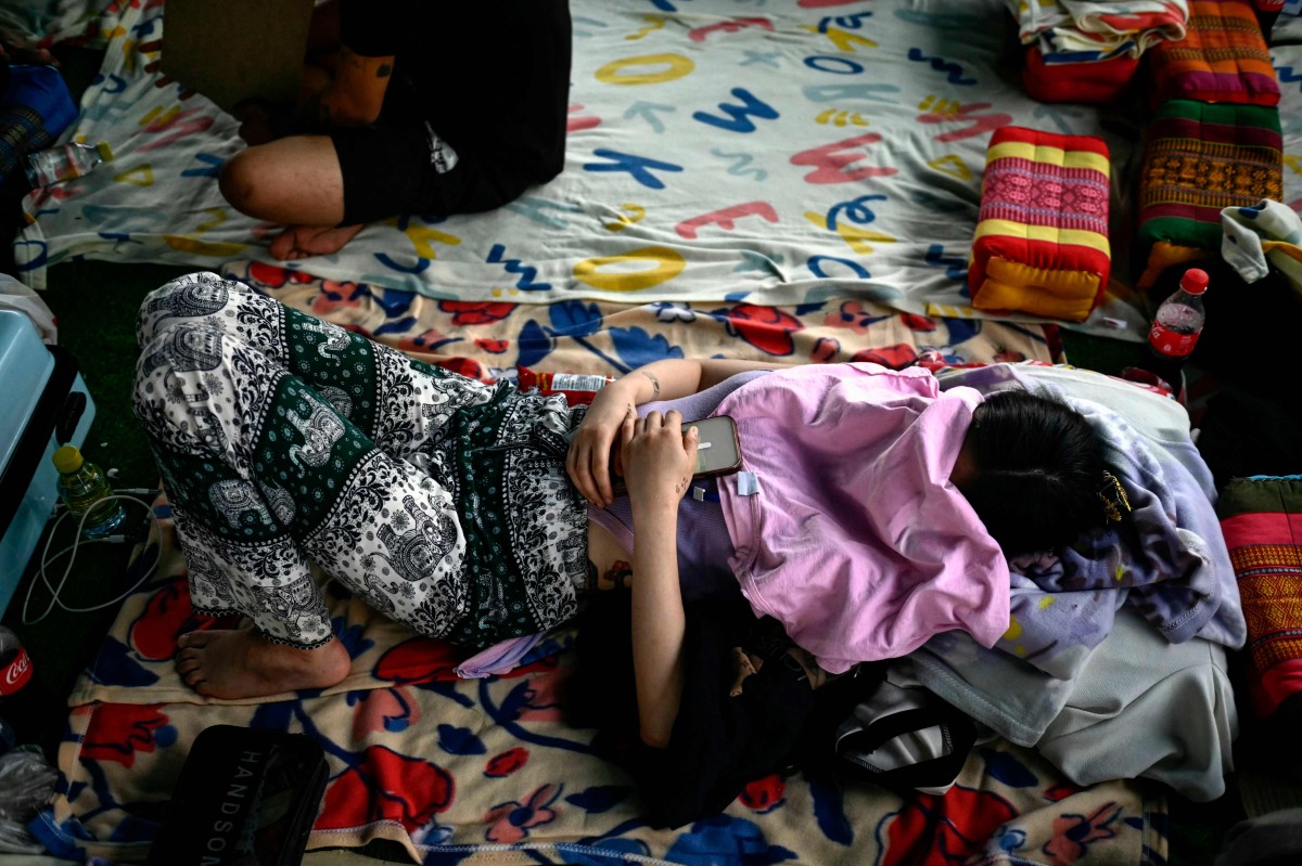 In this photo taken on February 23, 2025 alleged scam centre workers and victims rest during a crackdown operation by the Karen Border Guard Force (BGF) on illicit activity, at the border checkpoint with Thailand in Myanmar's eastern Myawaddy township. (Photo by AFP)
