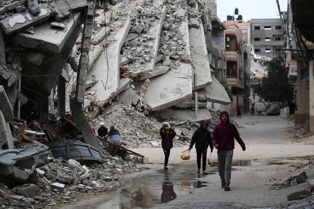 People walk past a building destroyed during Israeli strikes at the Nusseirat refugee camp, on March 20, 2025. Photo by Eyad BABA / AFP