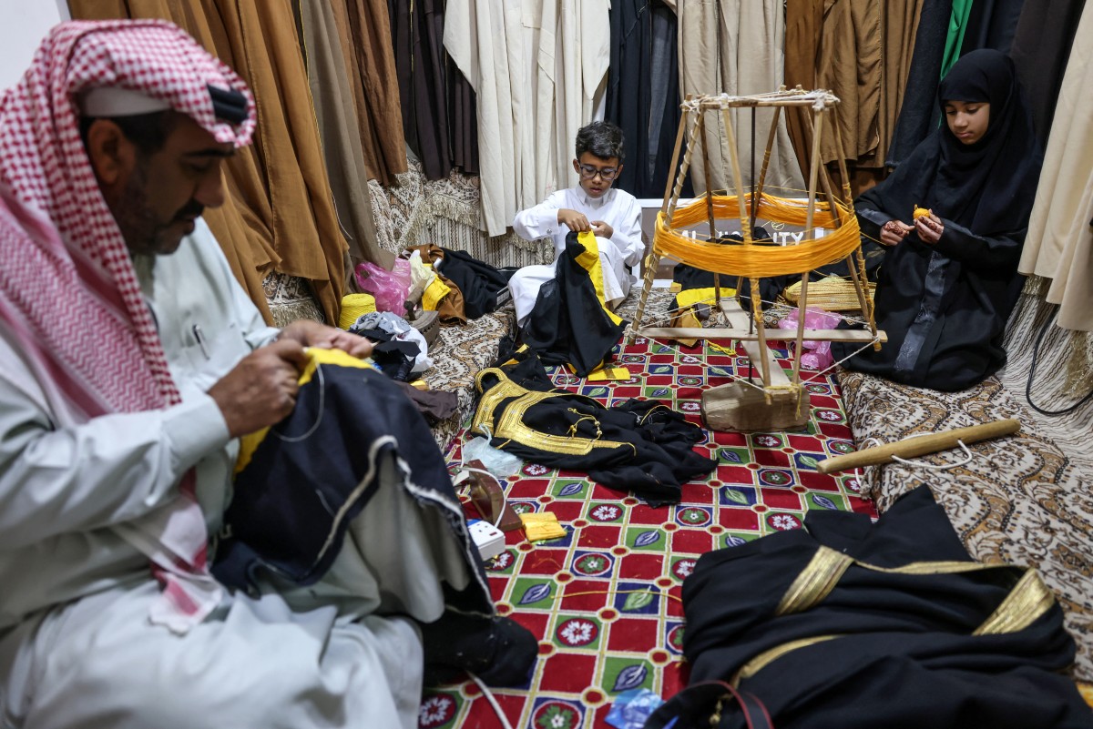 Saudi tailor Habib Mohammed (L) his grandson Ghassan and his granddaughter Fajr, work on bishts, inside Mohammed's workshop in the oasis city of Hofuf, in Saudi Arabia on February 16, 2025. (Photo by Fayez Nureldine / AFP)
