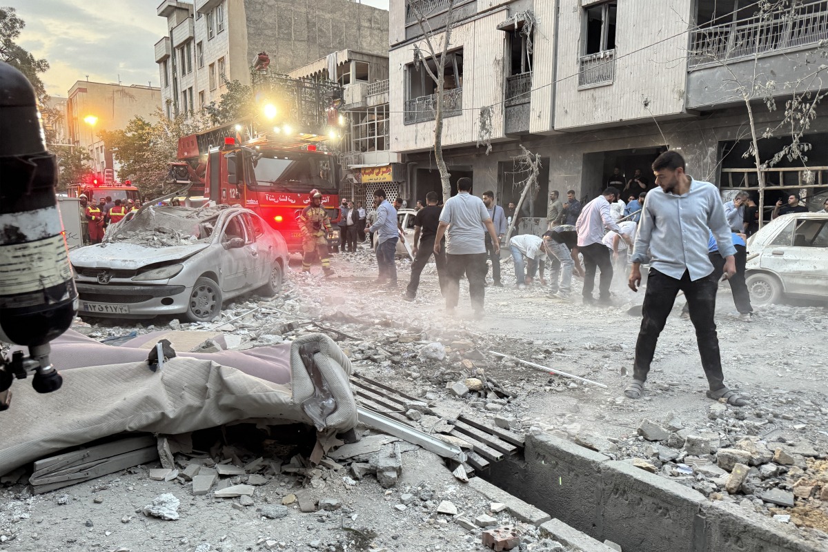 People and first-responders gather outside a building that was hit by an Israeli strike in Tehran on June 13, 2025. Photo by MEGHDAD MADADI / TASNIM NEWS / AFP.
