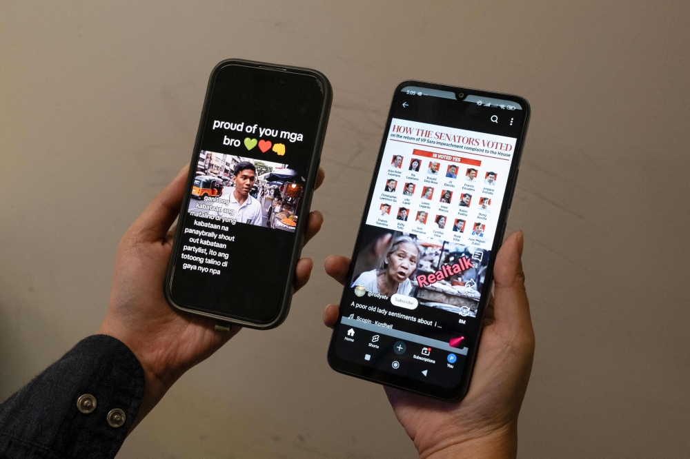 This photo illustration taken in Hong Kong on June 20, 2025 shows a person holding two mobile phones with two viral AI-generated videos of students and an old woman voicing their opinions on the impeachment of Philippine Vice President Sara Duterte. (Photo by Yan Zhao / AFP) 