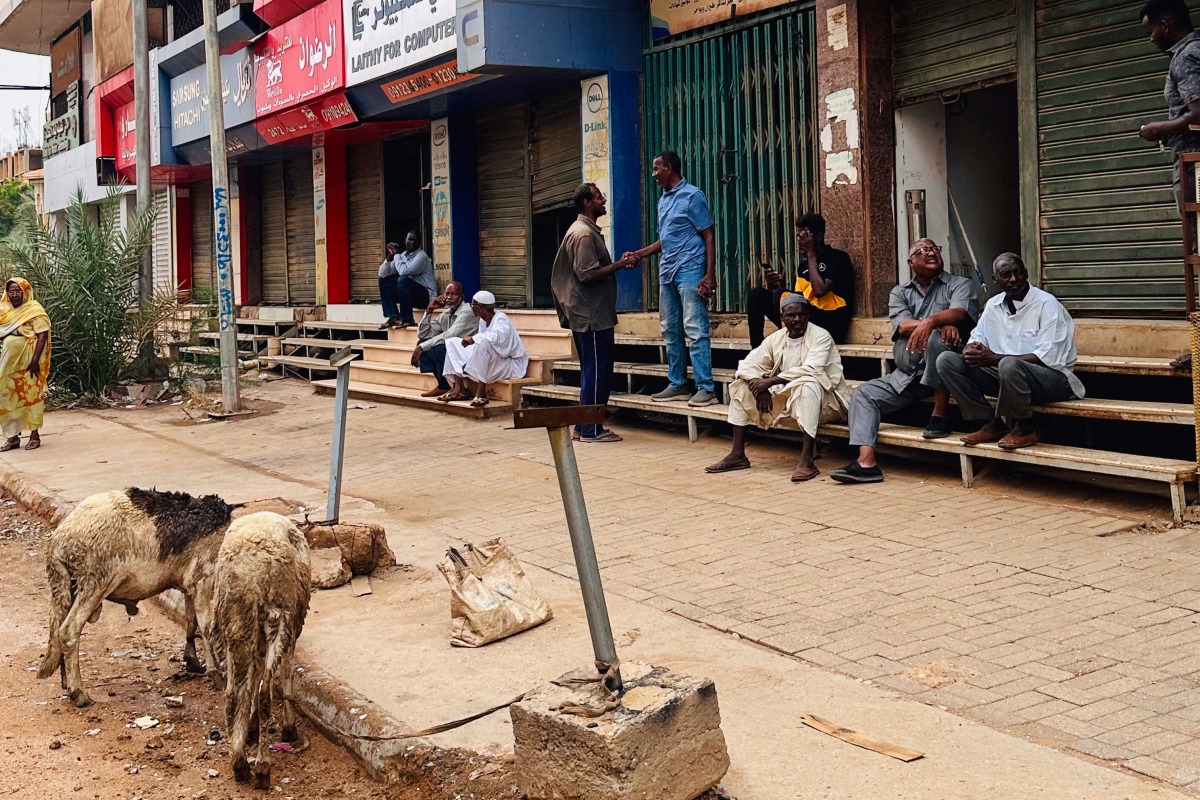 People sit on stairs outside shuttered stores at al-Hurriya street, a popular destination to buy electric home appliances before the Sudan war, as the shopping street reopens at al-Arabi market in Khartoum on July 15, 2025. (Photo by AFP)
