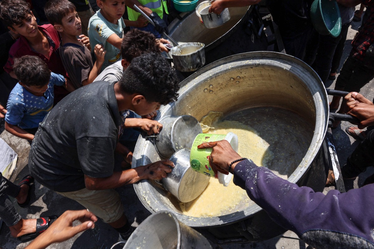 Displaced Palestinians try to take what remains in a pot of lentil soup at a food distribution point in Gaza City in the northern Gaza Strip on July 25, 2025. (Photo by Omar AL-QATTAA / AFP)
