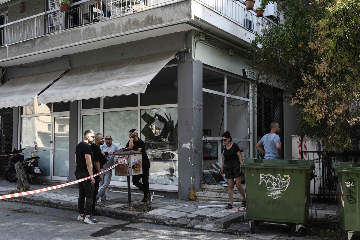 People stand next to a damaged shop following a strong blast in Thessaloniki on July 26, 2025. (Photo by Sakis Mitrolidis / AFP)
