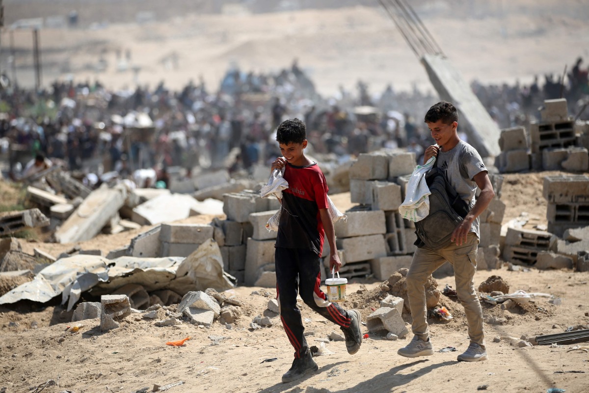 Palestinians return with bags from a food distribution point run by the US and Israeli-backed Gaza Humanitarian Foundation (GHF) group, near the Netsarim corridor in the central Gaza Strip on August 3, 2025. Photo by Eyad BABA / AFP