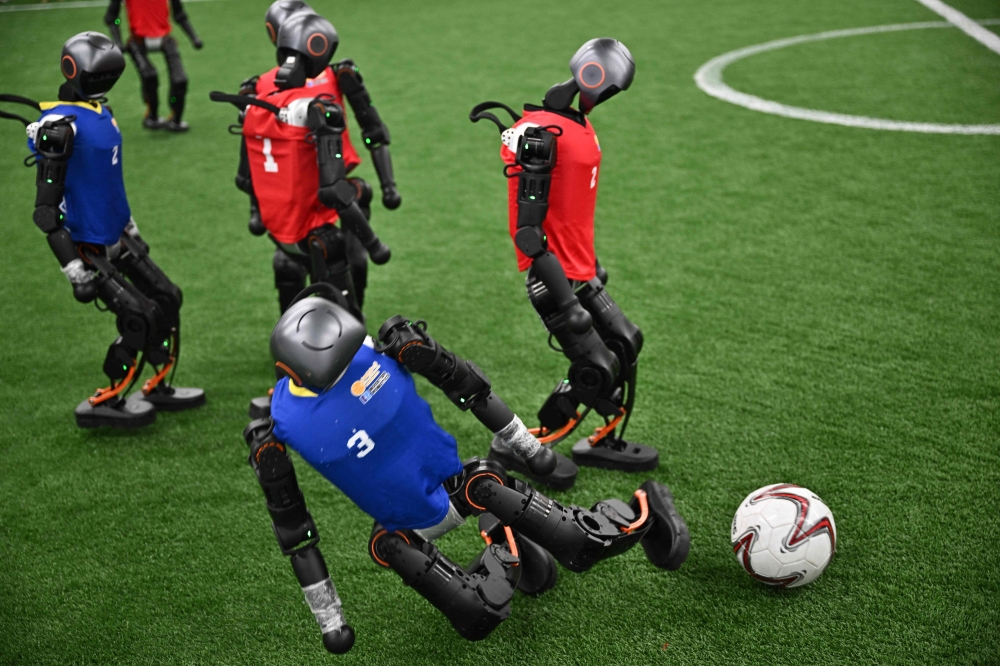 Humanoid robots vie for the ball during an exhibition football match ahead of the World Humanoid Robot Games in Beijing on August 4, 2025. (Photo by Pedro Pardo / AFP)