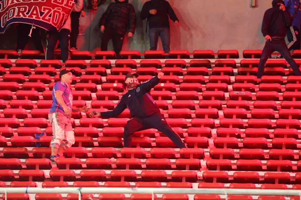 A fan of Universidad de Chile prepares to throw a stone during the Copa Sudamericana round of 16 second leg football match between Argentina's Independiente and Chile's Universidad de Chile on August 20, 2025. (Photo by Alejandro PAGNI / AFP)