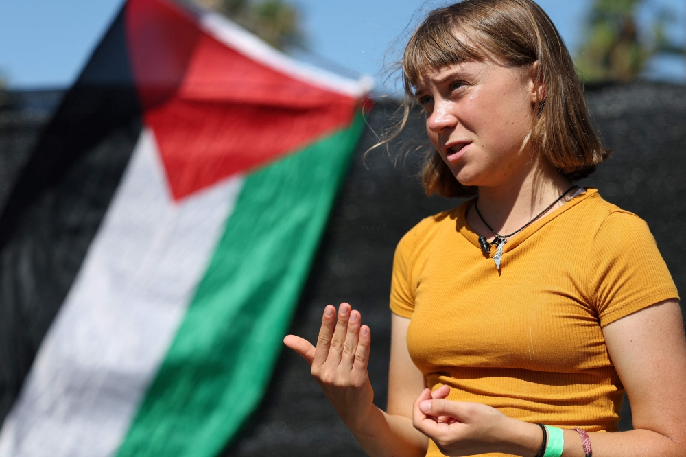 Swedish climate activist Greta Thunberg gestures while talking to media next to a Palestinian flag as a flotilla carrying humanitarian aid and activists prepare to leave on August 30, 2025. (Photo by Lluis Gene / AFP)