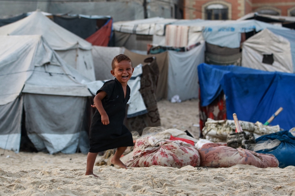 A displaced Palestinian child runs amid tents used as temporary shelter, in Deir el-Balah in the central Gaza Strip, on October 5, 2025. (Photo by Bashar Taleb / AFP)