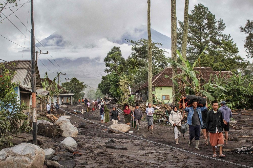 People walk on ground covered in volcanic ash after a pyroclastic flow during yesterday痴 eruption of Mount Semeru in Supiturang village, Lumajang, East Java on November 20, 2025. (Photo by Agus Harianto / AFP)
 