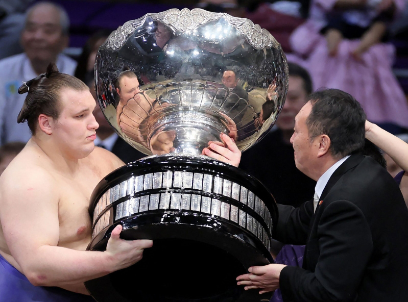Ukrainian sumo wrestler Danylo Yavhusishyn, also known by his Japanese ring name Aonishiki Arata (L), receives the Prime Minister's Cup trophy after winning the Grand Sumo Tournament in Fukuoka on November 23, 2025. (Photo by JIJI PRESS / AFP) 