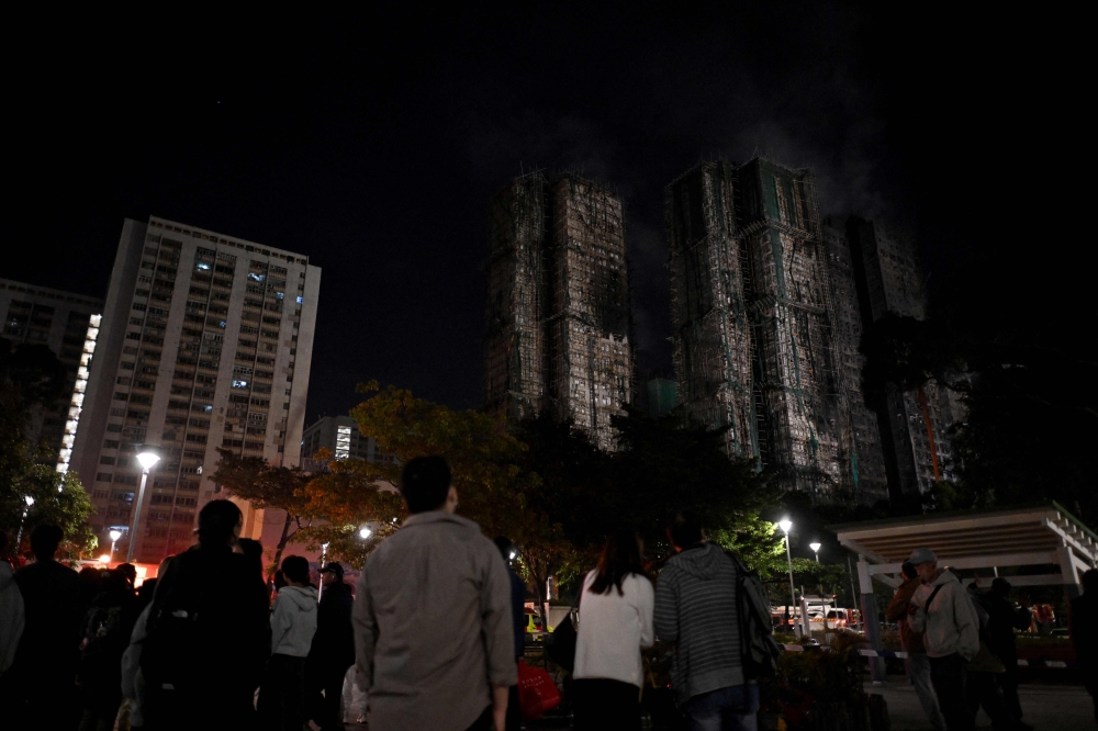 Bystanders look on after a major fire swept through several apartment blocks at the Wang Fuk Court residential estate in Hong Kong's Tai Po district on November 27, 2025. Residents anxiously awaited news of their loved ones on November 27 at a temporary shelter as one of Hong Kong's deadliest fires in decades engulfed a 2,000-unit high-rise complex. (Photo by Philip FONG / AFP)