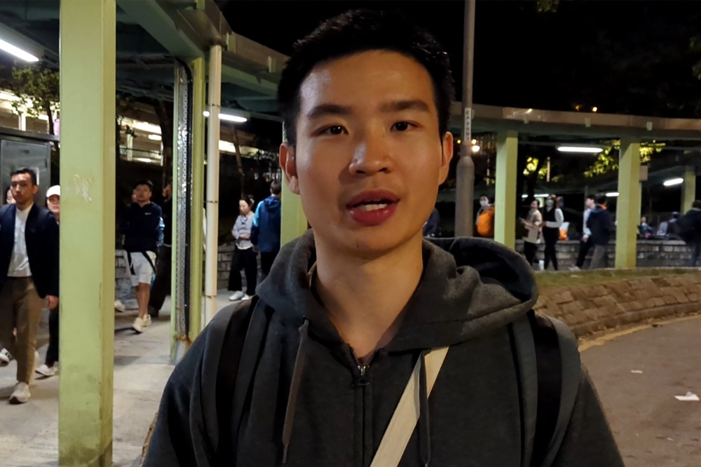 Miles Kwan, a 24-year-old student, speaks to AFP while handing out flyers outside a train station in Hong Kong's Tai Po district on November 28, 2025. (Photo by Holmes Chan / AFPTV / AFP)