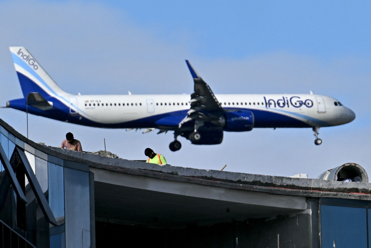 Labourers work atop an under-construction building as an Indigo aircraft prepares to land at Kempegowda International Airport in Bengaluru on December 4, 2025. Photo by Idrees MOHAMMED / AFP