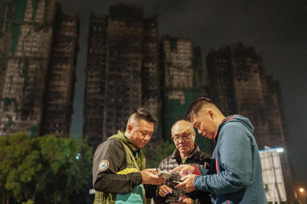 This picture taken on December 10, 2025 shows Yip Ka-kui (C) and his sons Yip Shun-ting (L) and Yip Shun-yin (R) looking at old photographs of his wife Pak Shui-lin. (Photo by Yan Zhao / AFP)