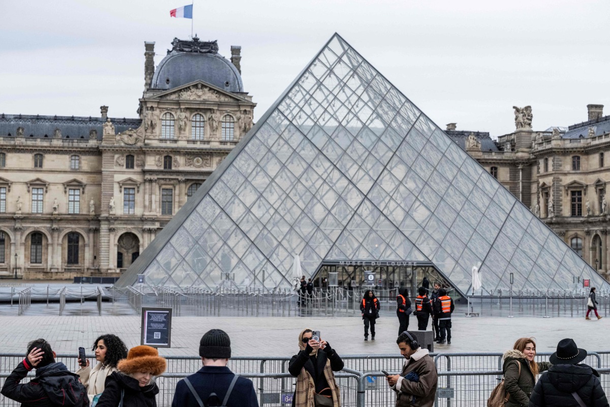 Tourists stand behind barriers blocking the access to the Louvre main courtyard, La Cour Napoleon, with the Louvre Pyramid, designed by Chinese-US architect Ieoh Ming Pei, as the Louvre Museum is closed due a strike, in Paris, on January 12, 2026. Photo by Martin LELIEVRE / AFP