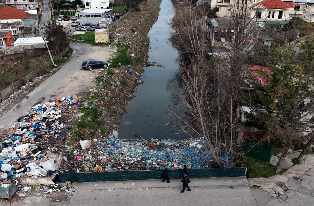 (Files) Local residents walk on a bridge, above plastic trash-filled floodwaters following heavy rains, in Durres, on January 13, 2026. (Photo by Adnan Beci / AFP)