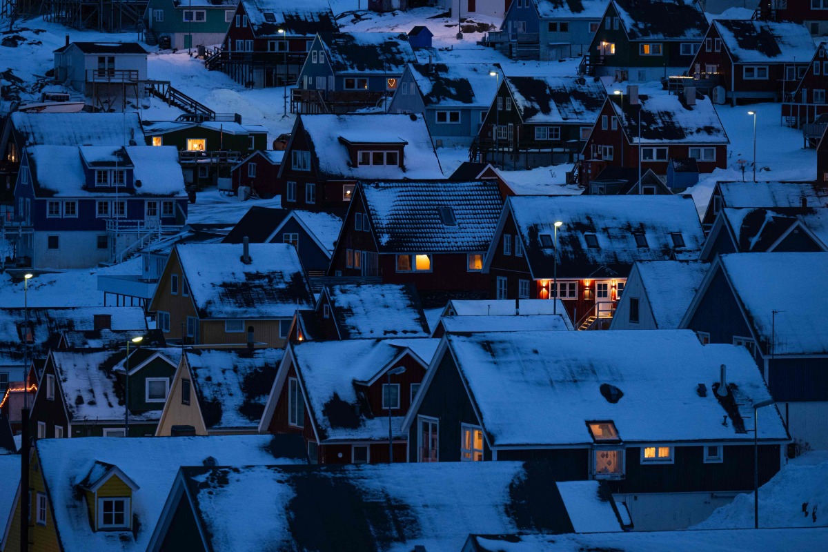 Houses along the coastline are lit as early morning light breaks over the snow-covered hills in Nuuk, Greenland, on January 22, 2026. (Photo by Jonathan NACKSTRAND / AFP)
