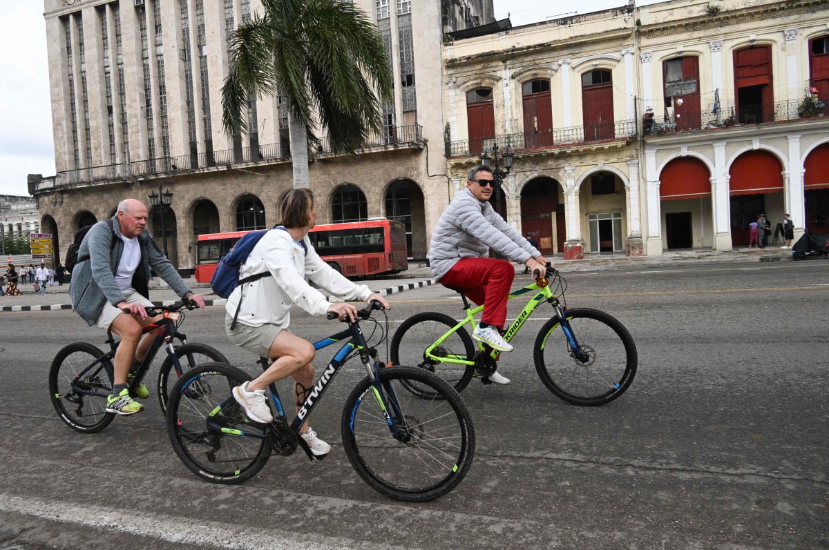 Tourists ride bicycles along a street in Havana on February 2, 2026. (Photo by YAMIL LAGE / AFP)