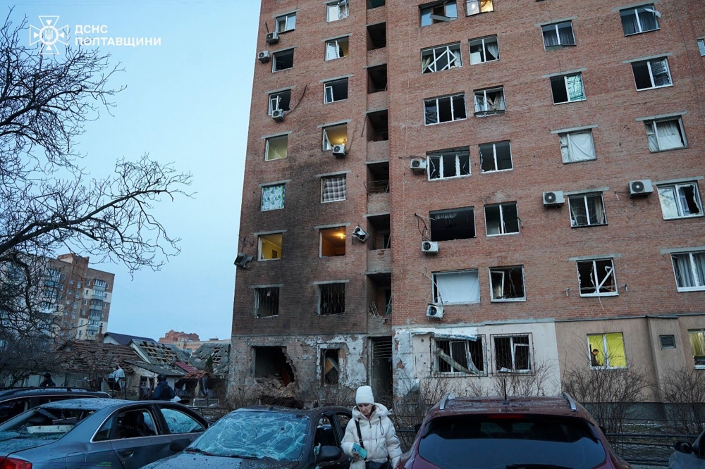 In this handout photograph taken and released by the Ukrainian Emergency Service on March 24, 2026, a woman walks past damaged cars in the courtyard of a damaged residential building following an air attack in Poltava, amid the Russian invasion of Ukraine. (Photo by Handout / Ukrainian Emergency Service / AFP)