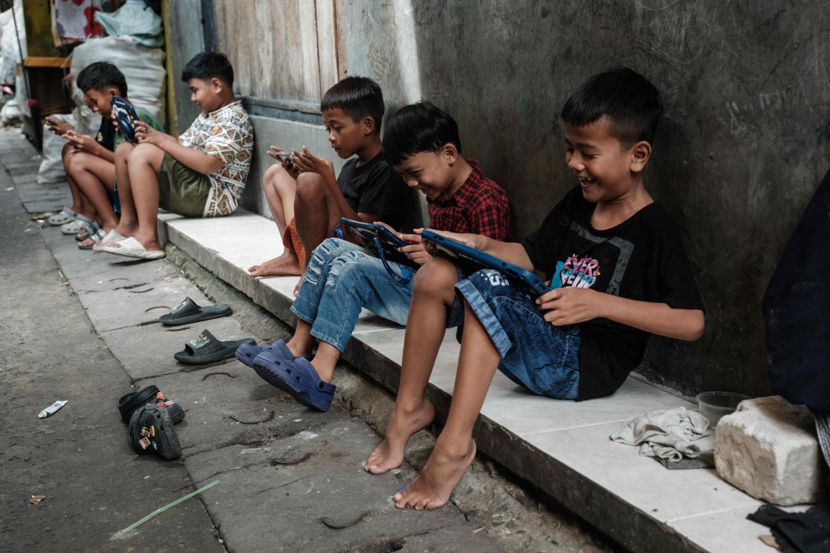 Children play online games against each other on smartphones and tablets along an alley in Jakarta on March 26, 2026. Photo by YASUYOSHI CHIBA / AFP